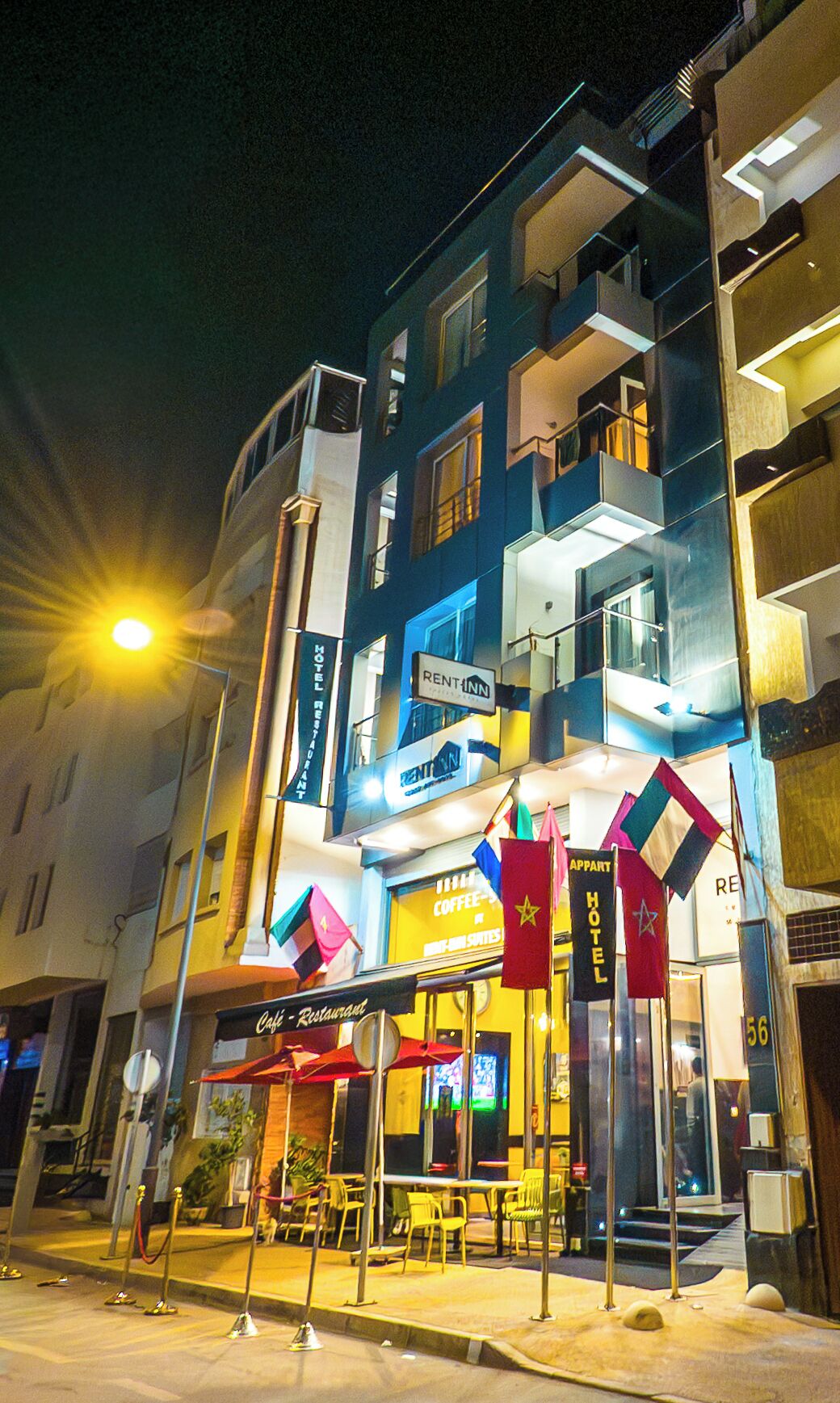 A multi-story building with a 'RENT-A-UNIT' sign, a 'Café-Restaurant' sign, and flags for 'HOTEL' and 'RENT-A-UNIT'.