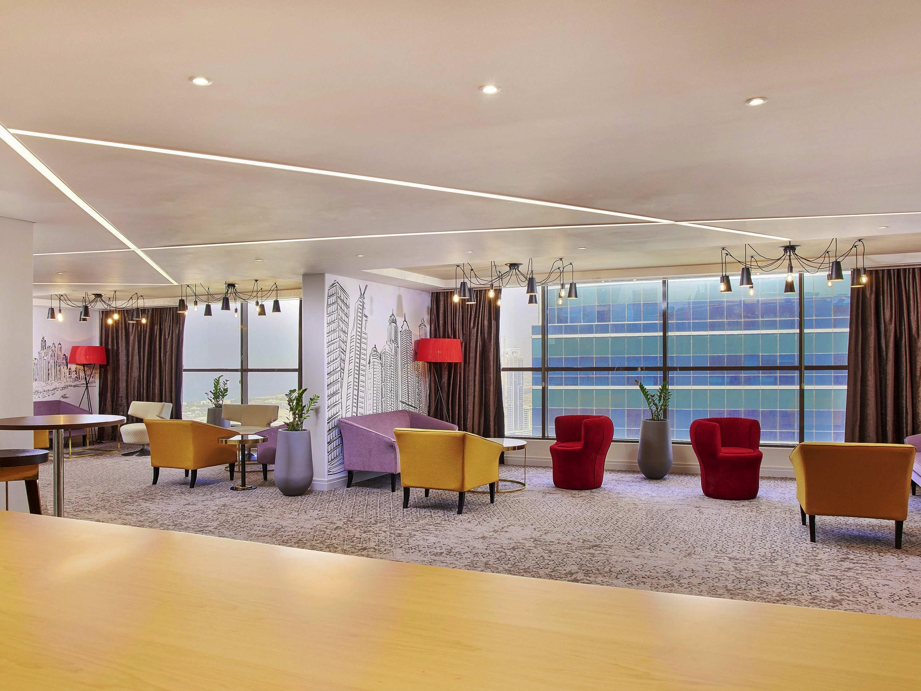 A modern hotel lobby with a seating area, a large window with a city view, and a decorative wall mural.