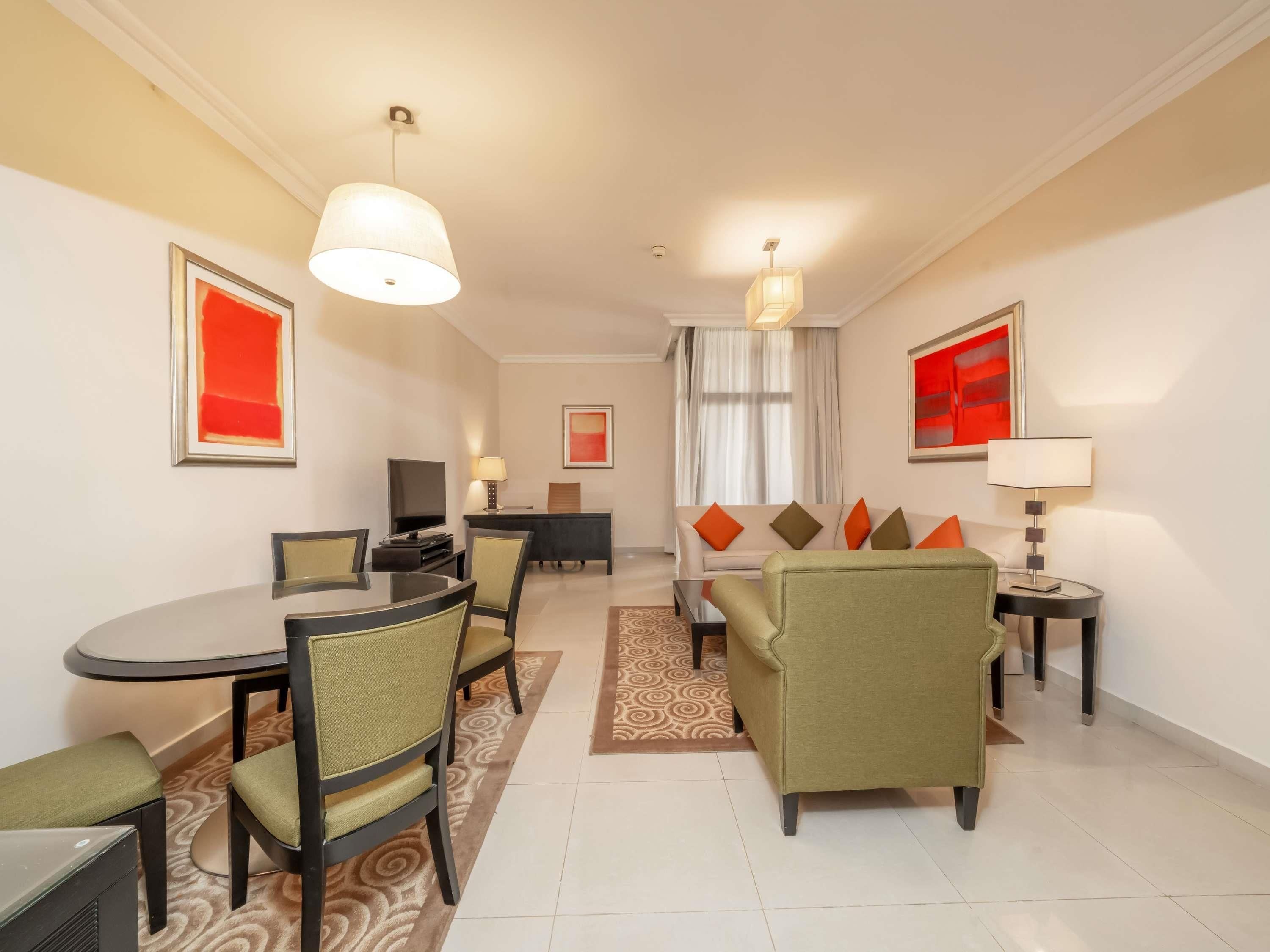 A hotel room with a dining area, a sofa set, a TV, and a desk.