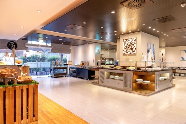 A modern hotel lobby with a central reception area, a buffet counter, and a seating area with tables and chairs.