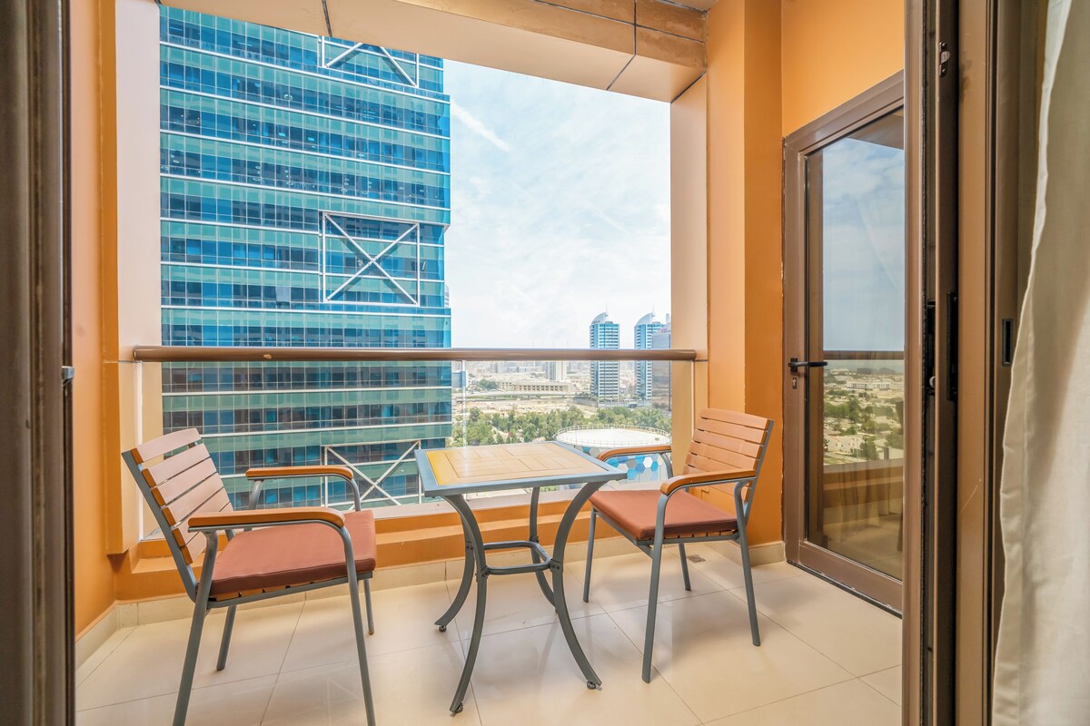 Un balcon avec une table et deux chaises, une vue sur un immeuble moderne et une porte vitrée.