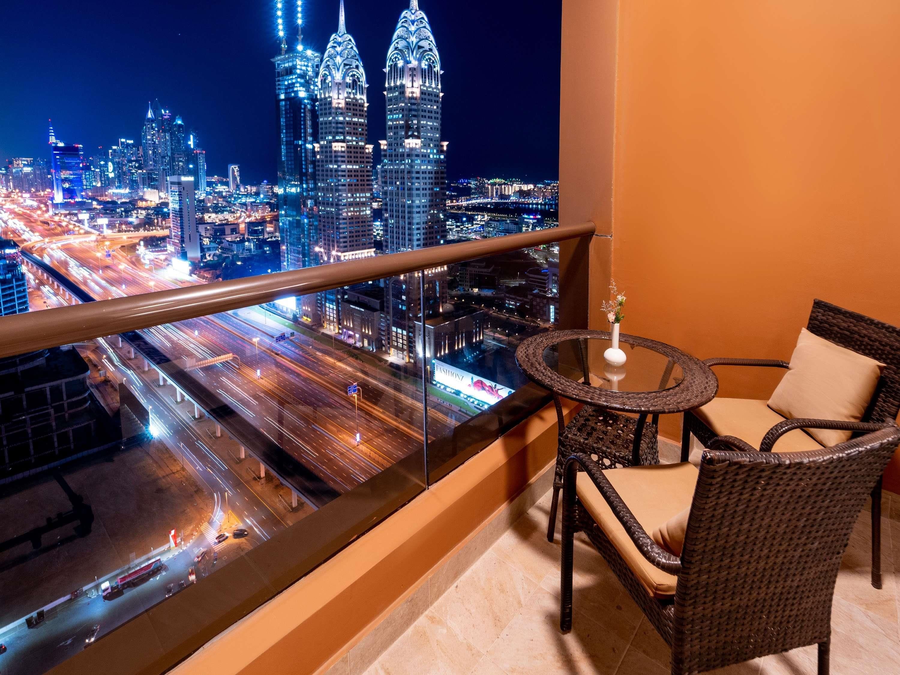 A balcony with a view of a cityscape at night, featuring illuminated skyscrapers and a busy road below.