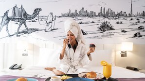 Une chambre d’hôtel avec une fresque représentant un paysage urbain, un plateau de petit-déjeuner avec des croissants, des œufs et du jus, et un téléphone sur la table de chevet.