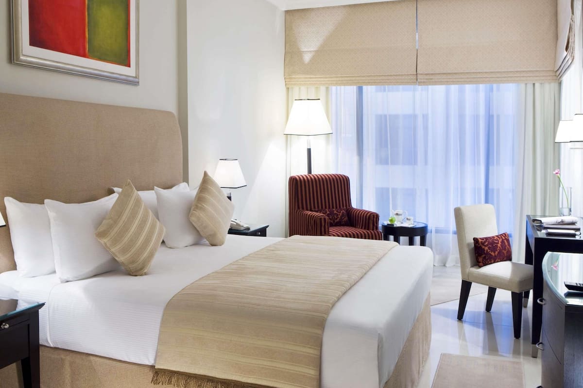 A hotel room with a large bed, two bedside tables, a chair, a desk, and a large window with curtains.