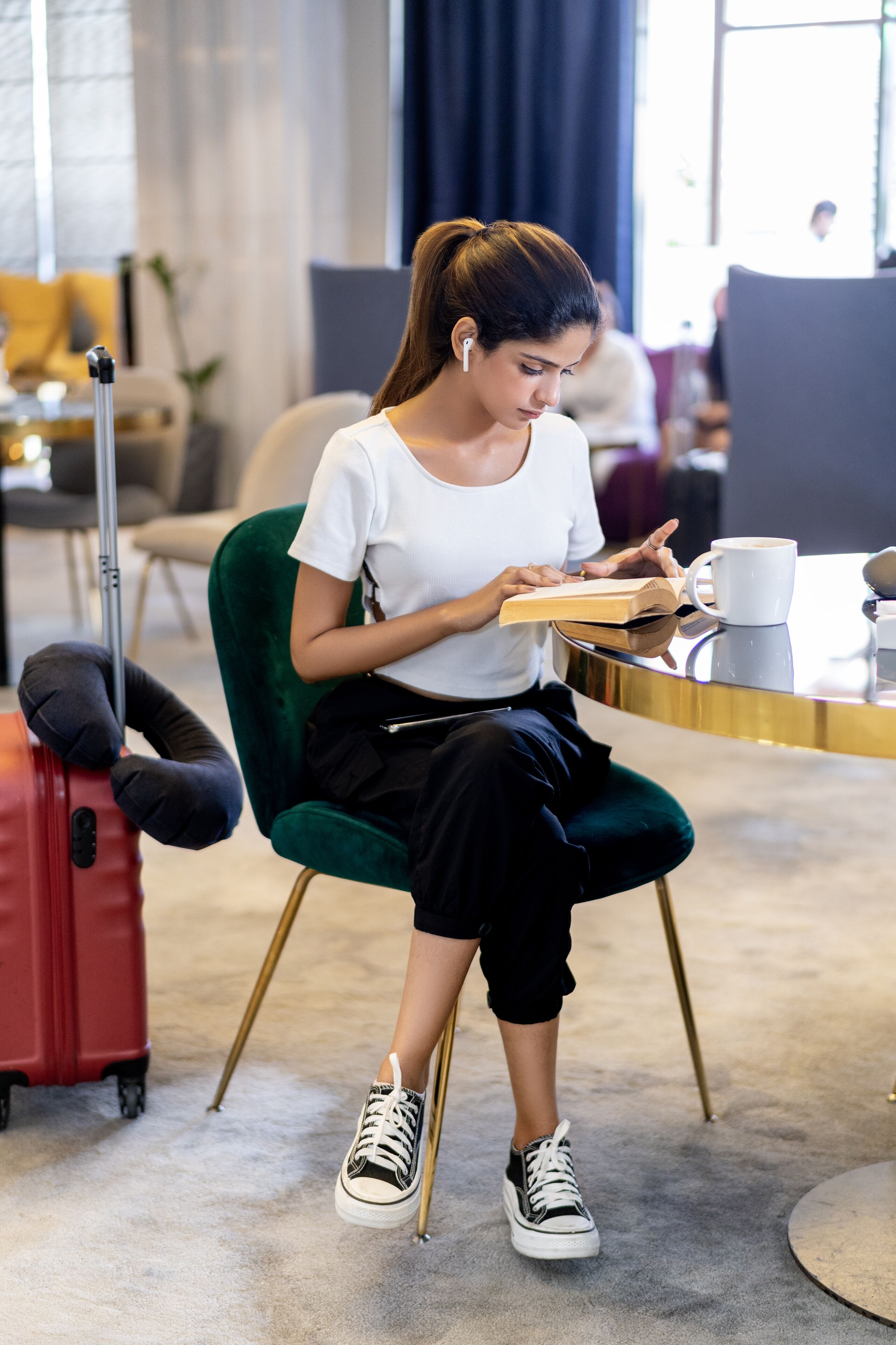 A person sitting at a table with a laptop, a cup, and a suitcase.