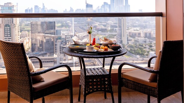 Un balcon avec des fauteuils en osier et une table ronde sur laquelle est disposée une variété de plats.