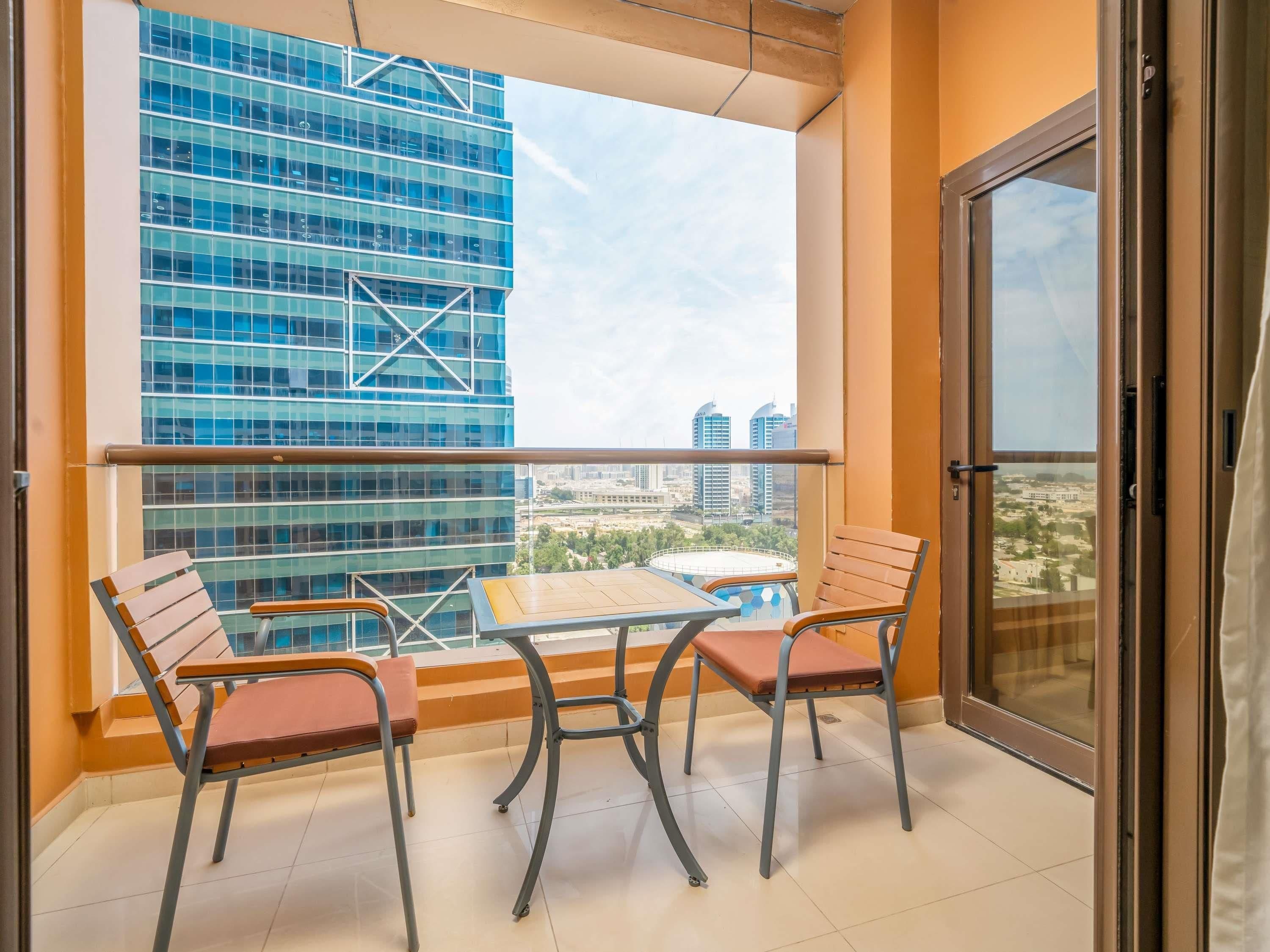 Un balcone con tavolo e sedie, vista su un edificio moderno e una porta vetrata.