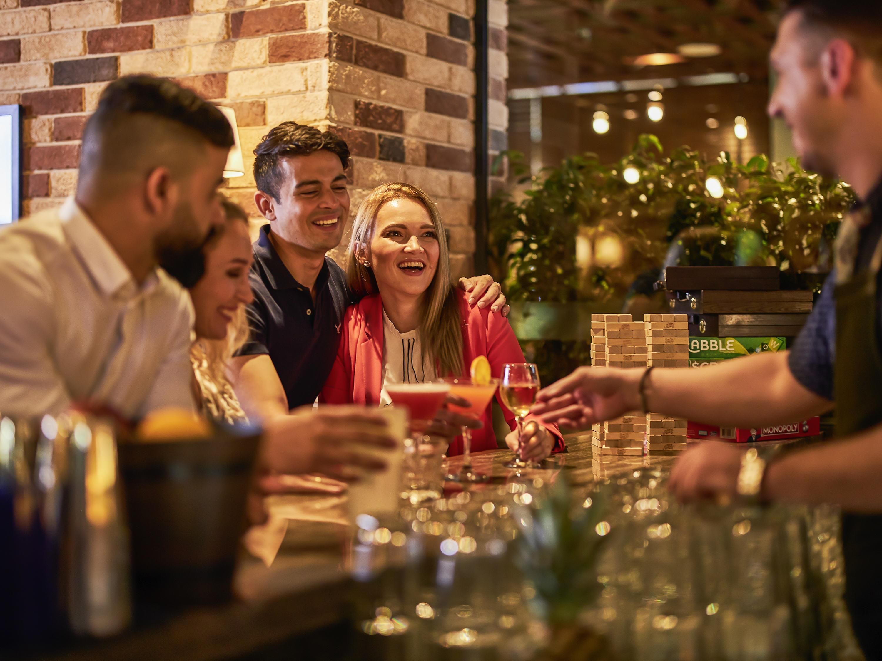 Un grupo de personas en un bar, con una pared de ladrillo y plantas de interior al fondo.