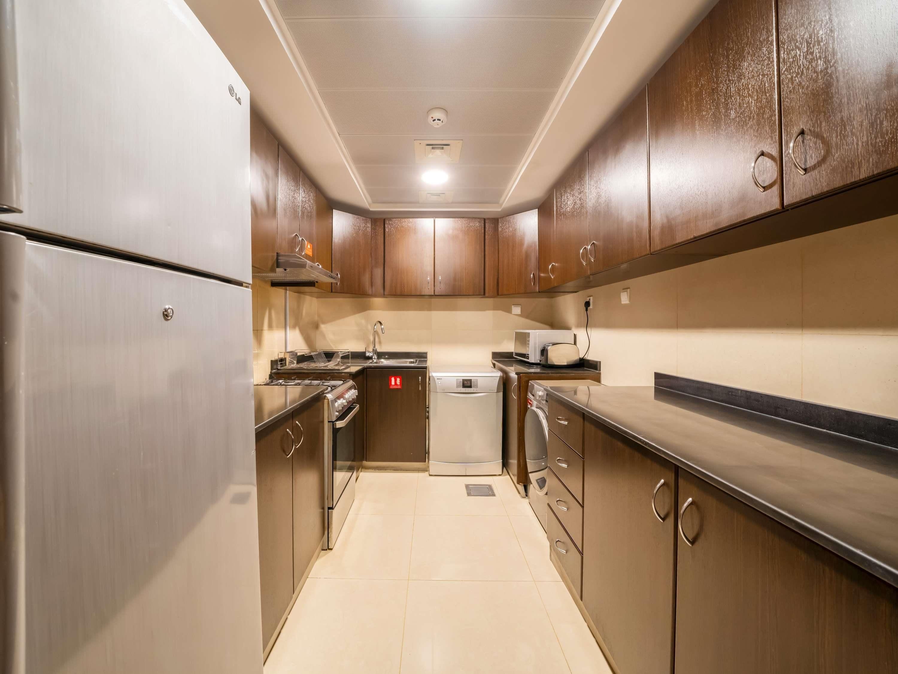 A compact kitchen with stainless steel appliances, wooden cabinets, and a tiled floor.