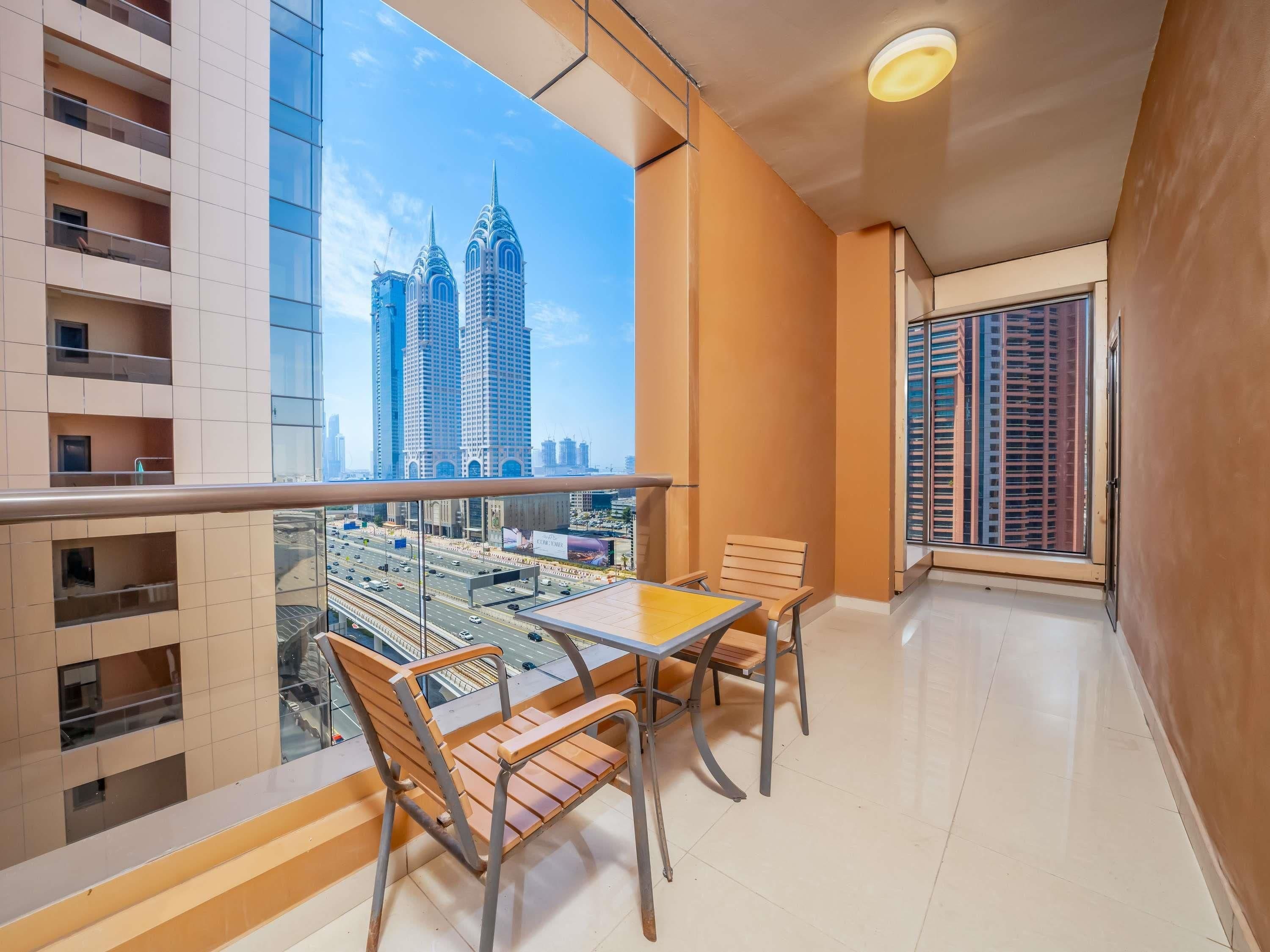 A balcony with a table and chairs, a view of tall buildings, and a clear sky.