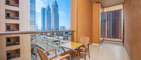 A balcony with a table and chairs, a view of tall buildings, and a clear sky.
