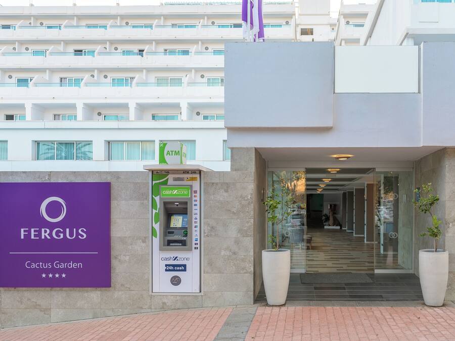 Ein Hotel Eingang mit einem Geldautomaten, der rund um die Uhr zugänglich ist, einem Schild für 'Fergus Cactus Garden' und einer modernen Gebäudefassade.