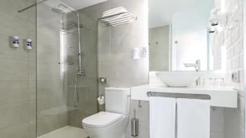 A modern bathroom with a glass-enclosed shower, a white toilet, and a sink with a large mirror above it.