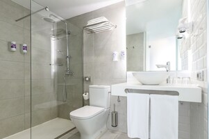 A modern bathroom with a glass-enclosed shower, a white toilet, and a sink with a large mirror above it.