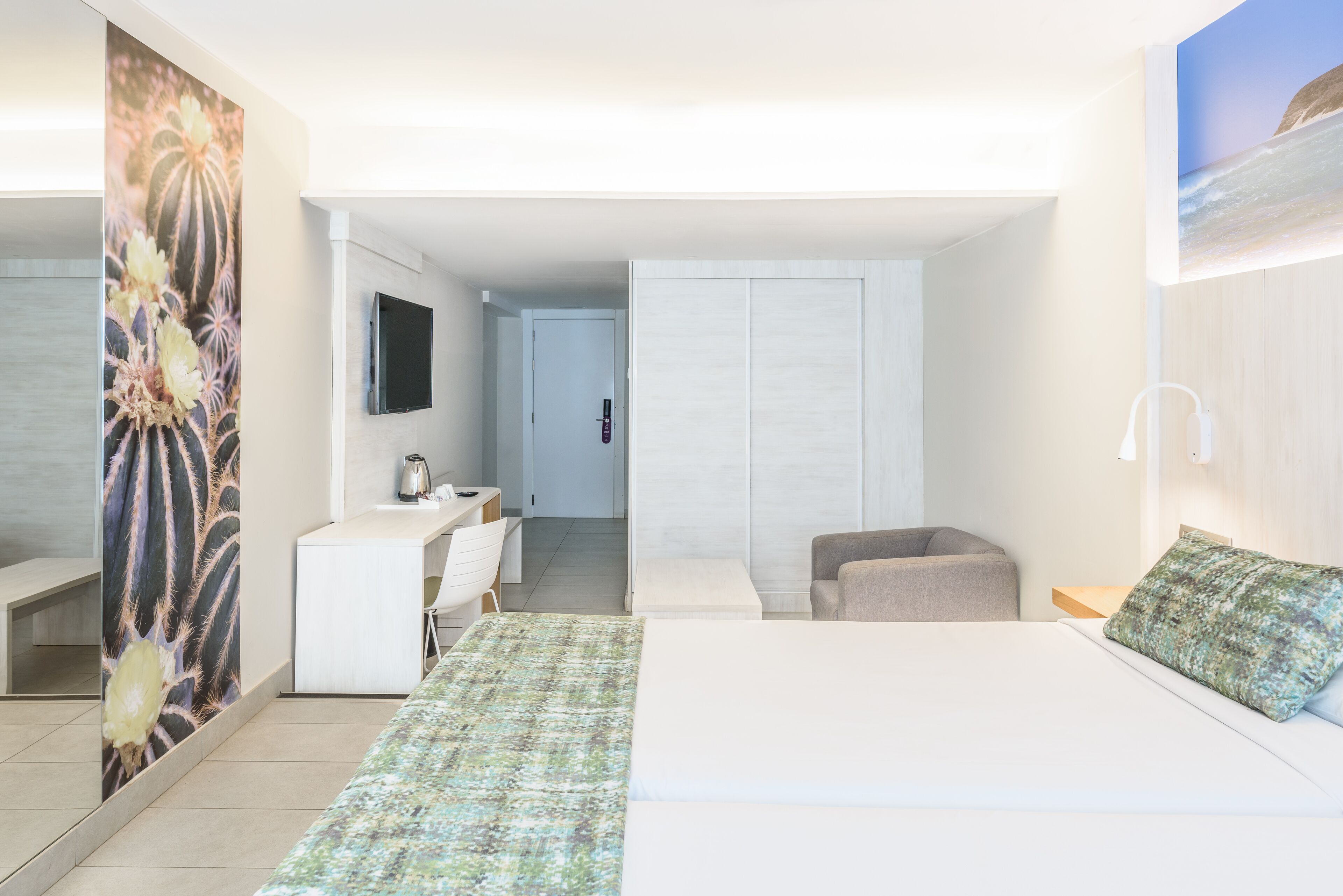 A modern hotel room with a bed, a desk, a chair, and a wardrobe.