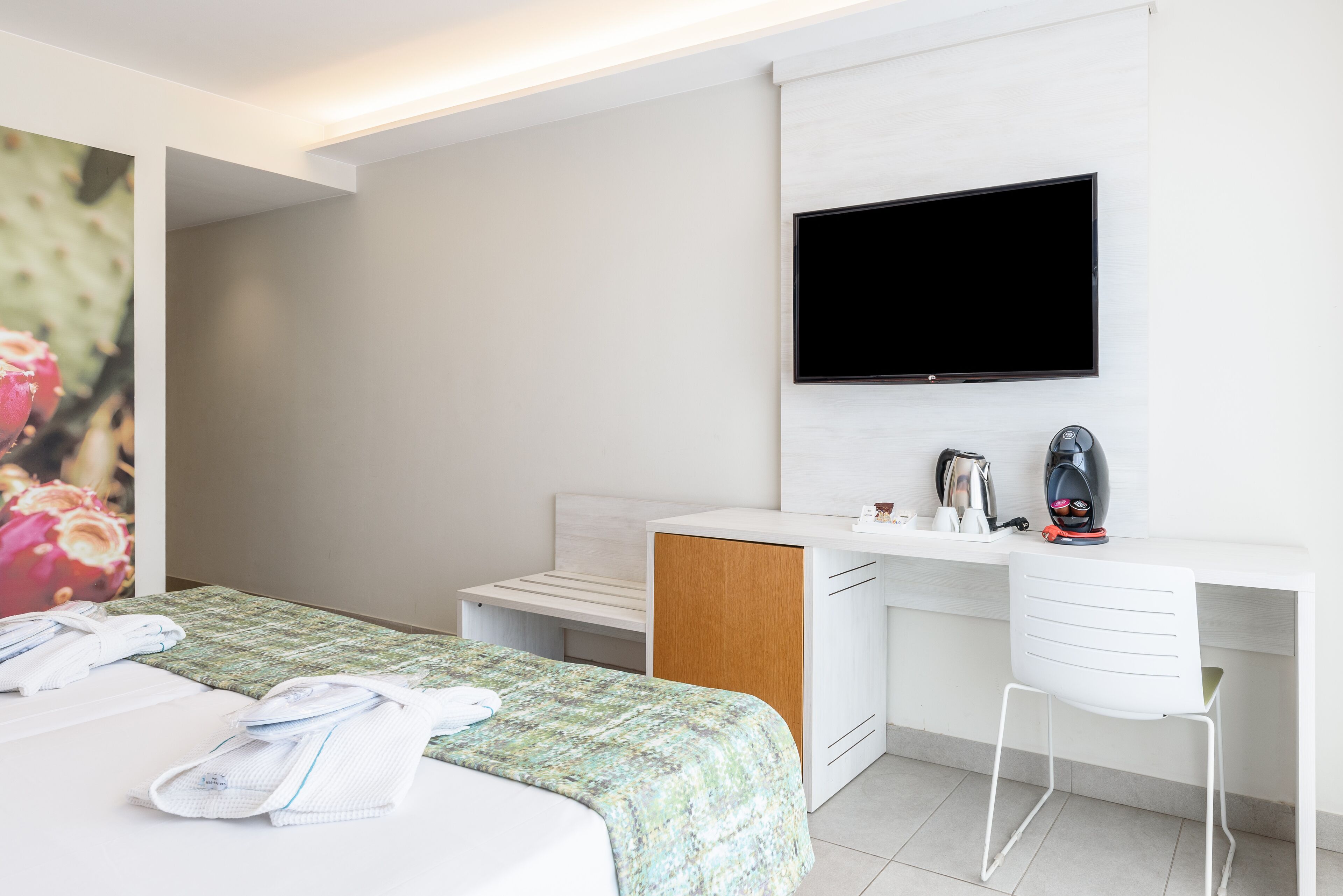 Una habitación de hotel moderna con cama, escritorio, silla, televisor de pantalla plana y cafetera.