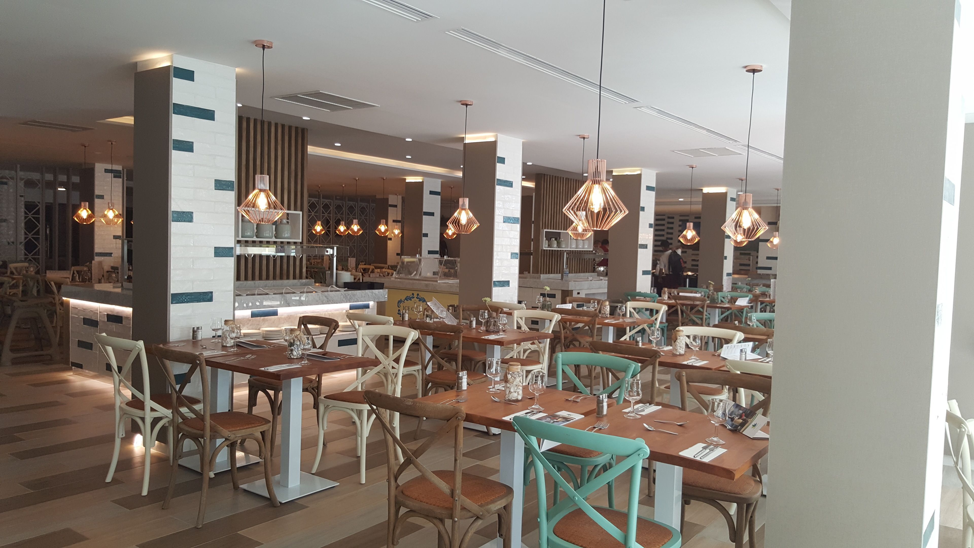 Un restaurante moderno con mesas y sillas de madera, iluminación colgante y una zona de bar.