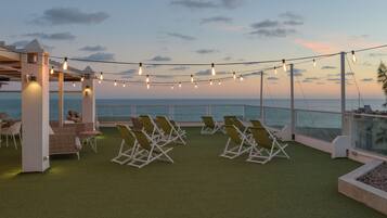 A rooftop terrace with lounge chairs, a pergola, and string lights.