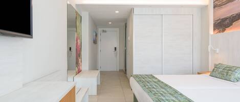 A hotel room with a bed, a TV mounted on the wall, a desk, and a wardrobe.