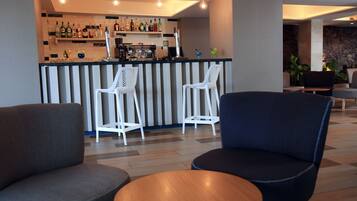 A bar area with white chairs and a counter stocked with various bottles.