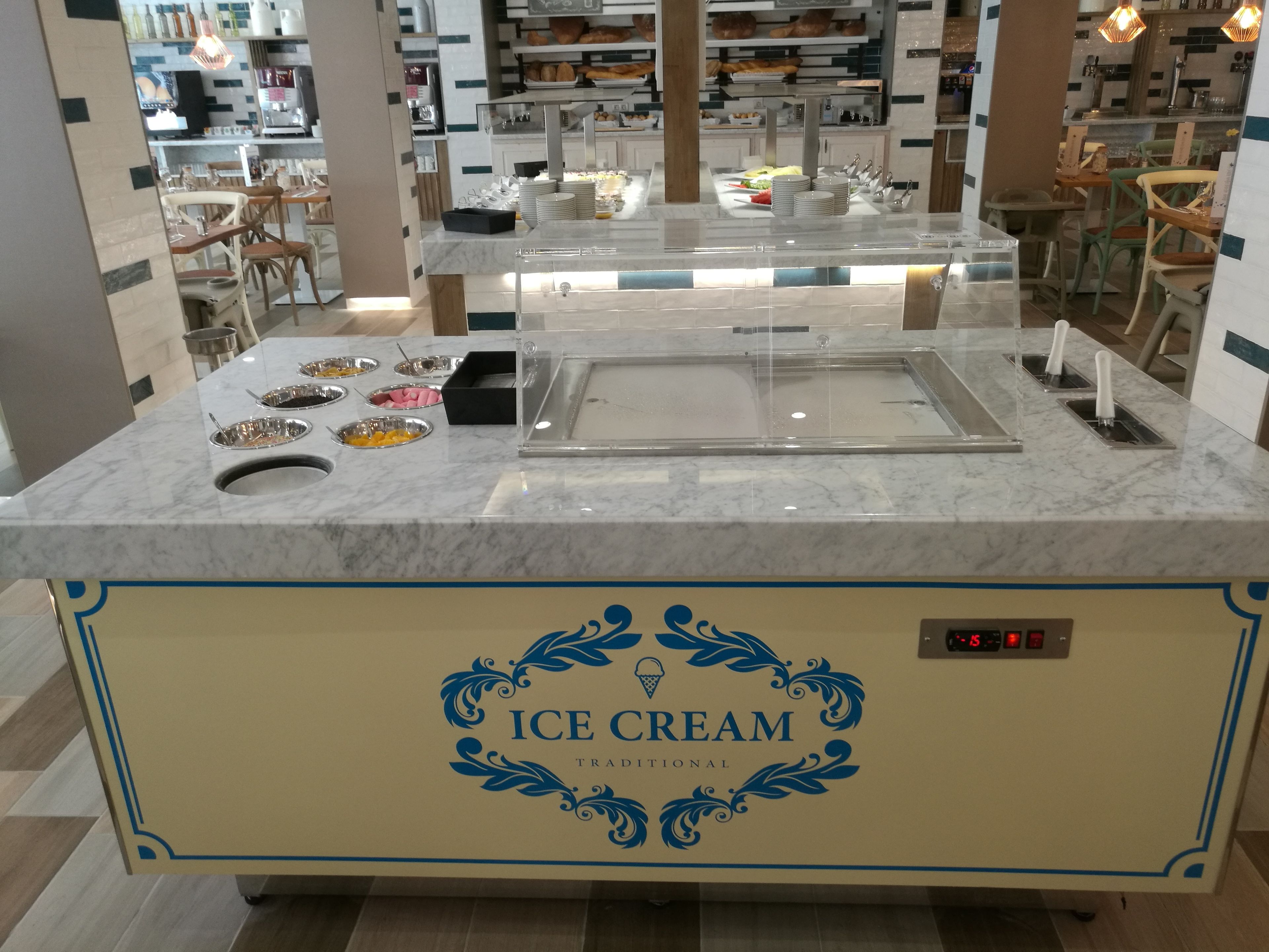 Un puesto de helados con pantalla digital, rodeado de asientos y una cocina al fondo.