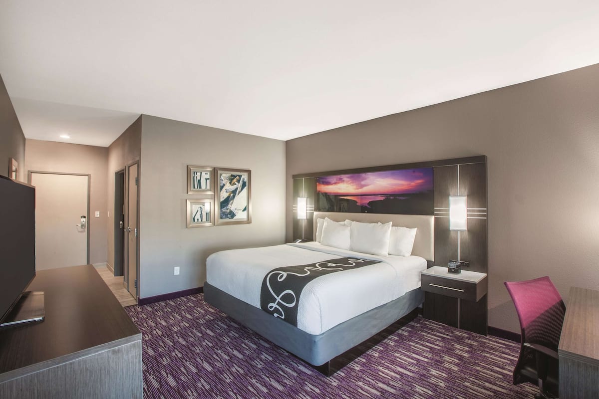 A hotel room with a large bed, a desk, a chair, a TV, and a painting on the wall.