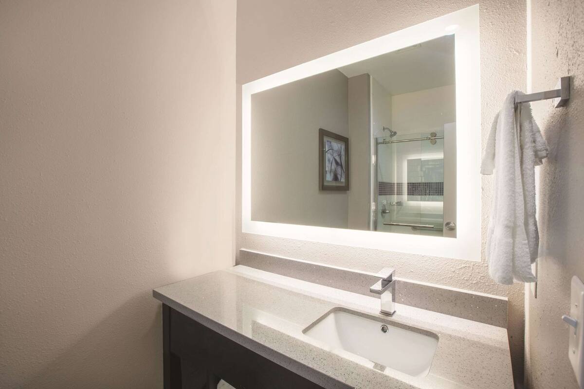 A bathroom with a large mirror, a sink, and a towel rack.