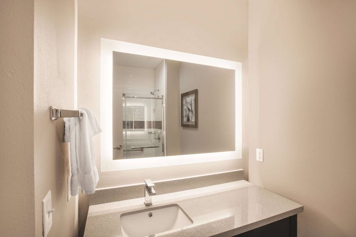 A bathroom with a large mirror, a sink, and a towel rack.