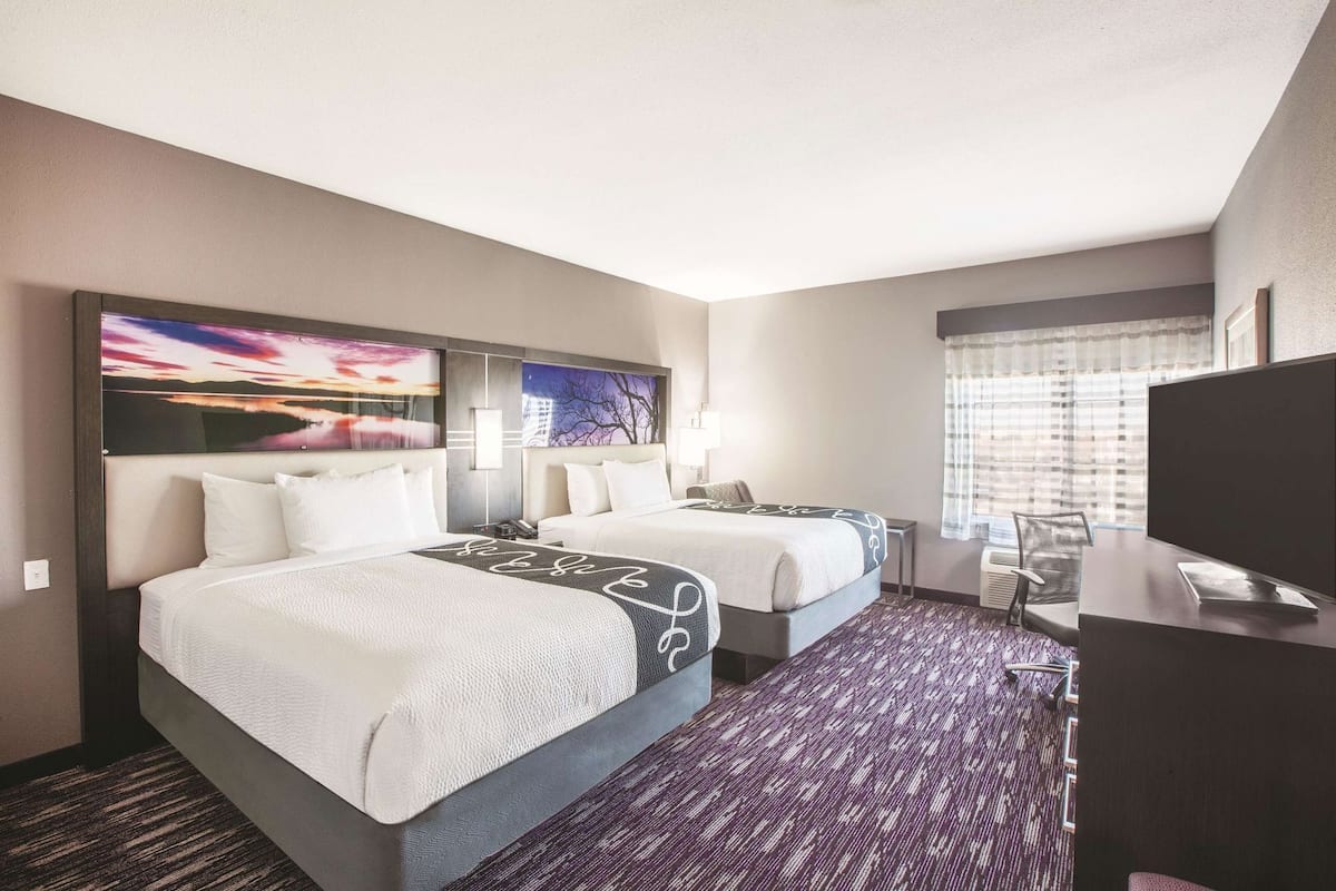 A hotel room with two beds, a desk, a TV, and artwork on the walls.