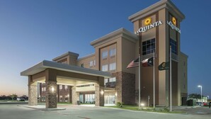 Un hotel La Quinta con un diseño moderno, que presenta una entrada destacada, un área exterior cubierta y una bandera estadounidense.