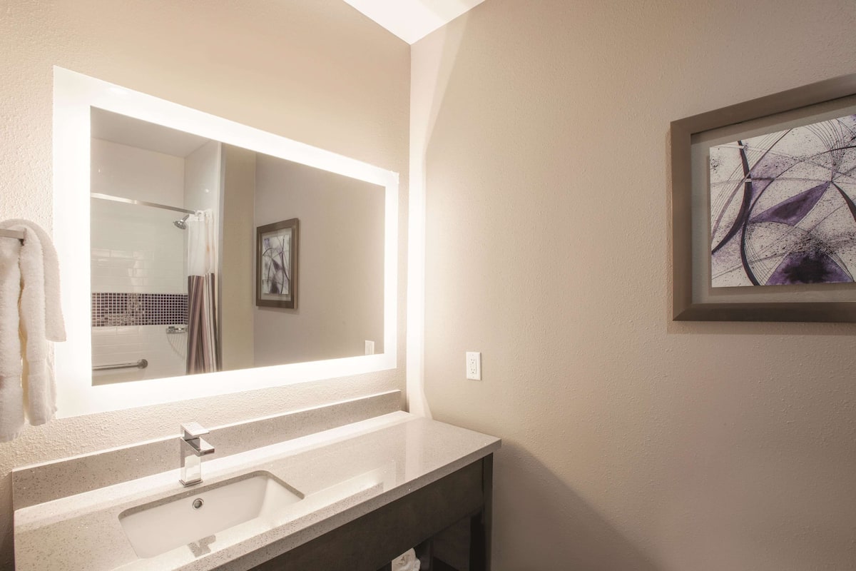 A modern bathroom with a large mirror, a sink, and a framed abstract painting on the wall.