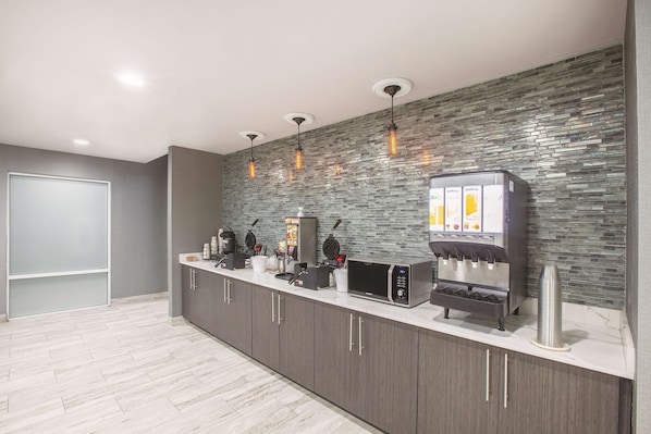 A modern kitchen area with a stone backsplash, a coffee machine, a waffle maker, and a microwave.