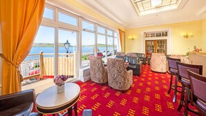 Quarto de hotel com uma janela grande, um tapete vermelho e uma varanda com vista para o mar.