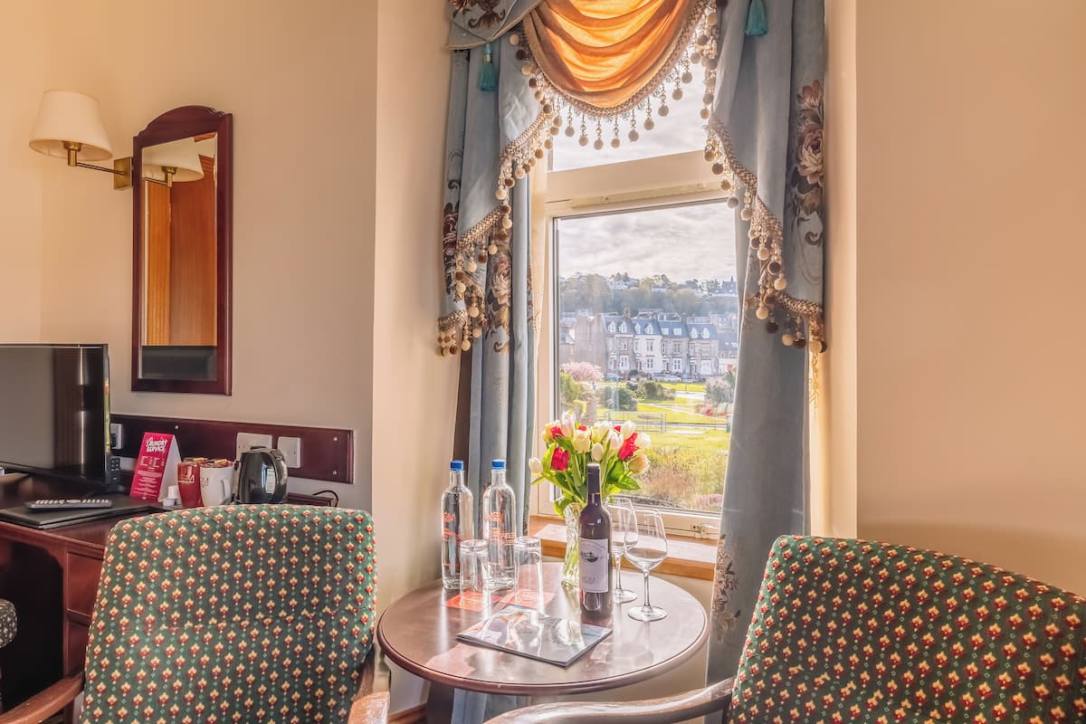 A hotel room with a dining table, two chairs, a mirror, a TV, and a view of a cityscape.