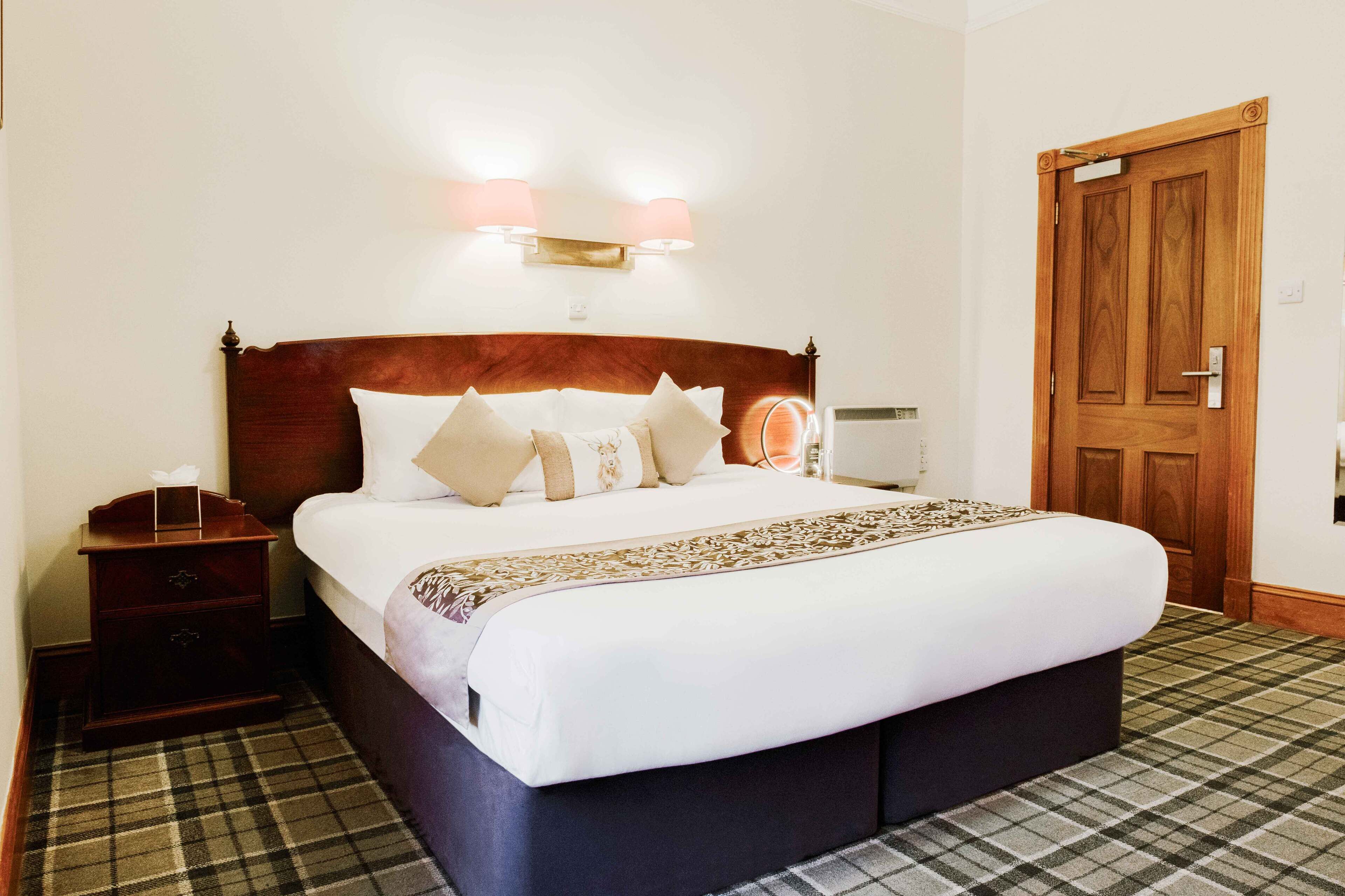 A neatly made bed with a headboard, a bedside table with a lamp, and a door to the right.