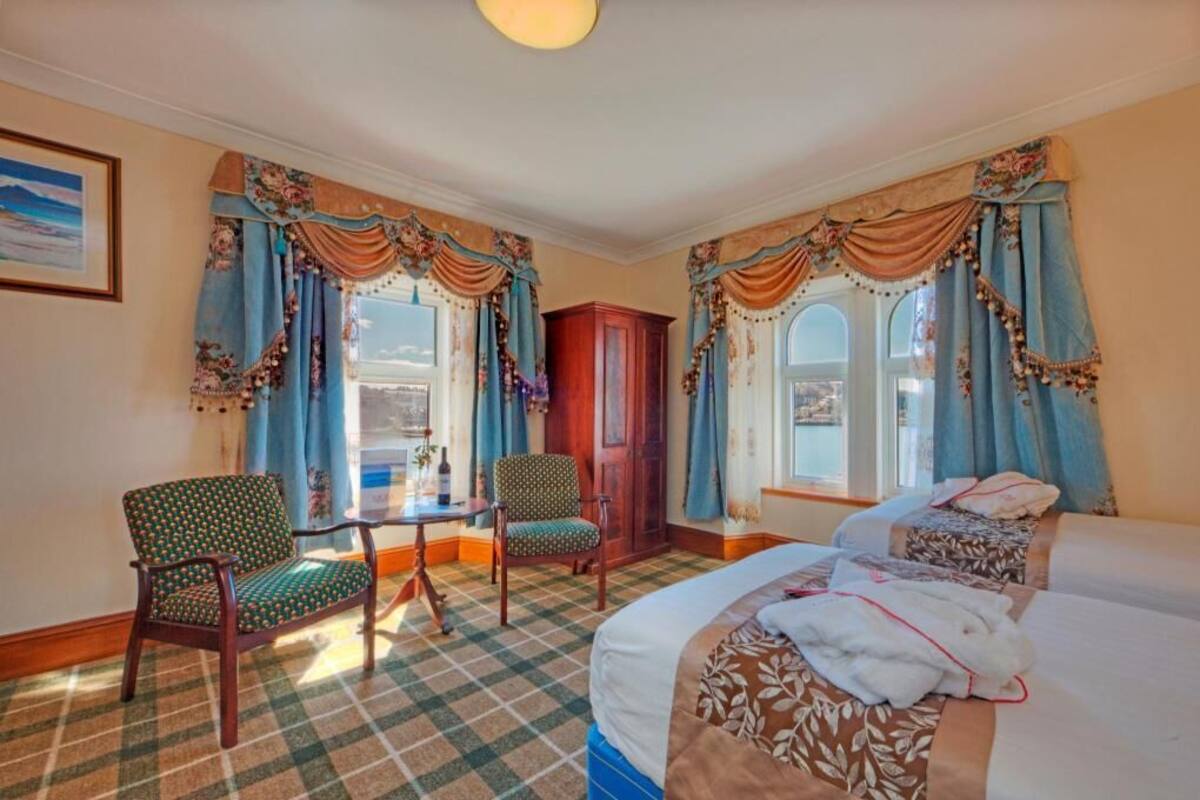 A hotel room with a checkered floor, two beds, a table with chairs, and curtains.