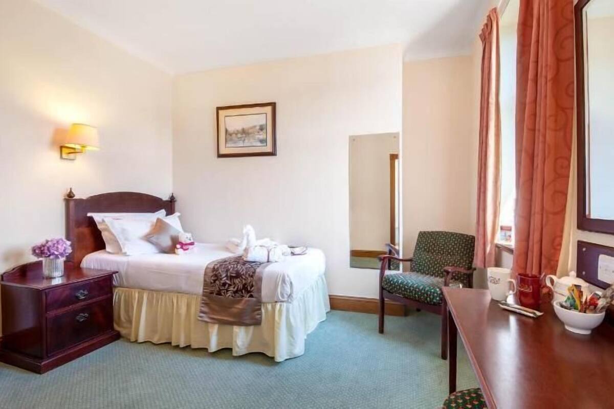 A hotel room with a bed, bedside table, chair, and a desk with a bowl.