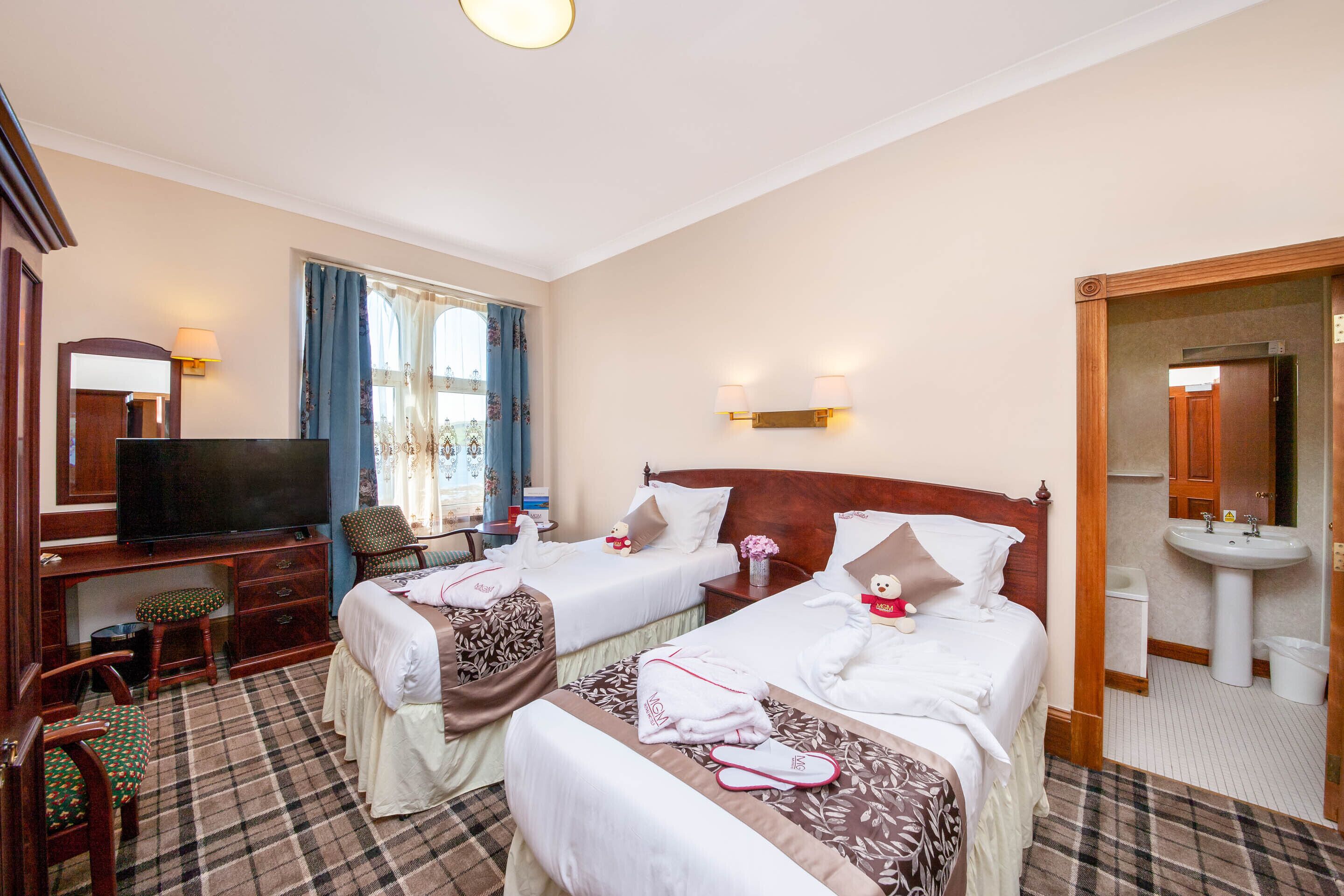 A hotel room with two beds, a television, a desk, and a bathroom.