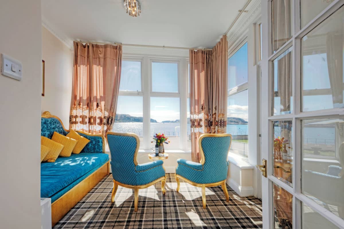 A room with a blue sofa, two matching chairs, a checkered floor, and large windows with curtains.