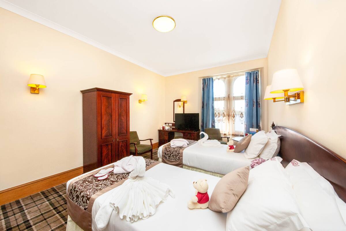 A hotel room with two beds, a wardrobe, a television, and a window with curtains.