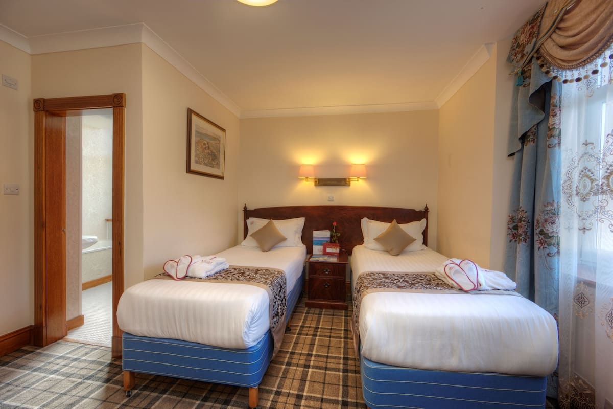 A hotel room with two beds, a wooden headboard, a nightstand, and a bathroom visible through an open door.