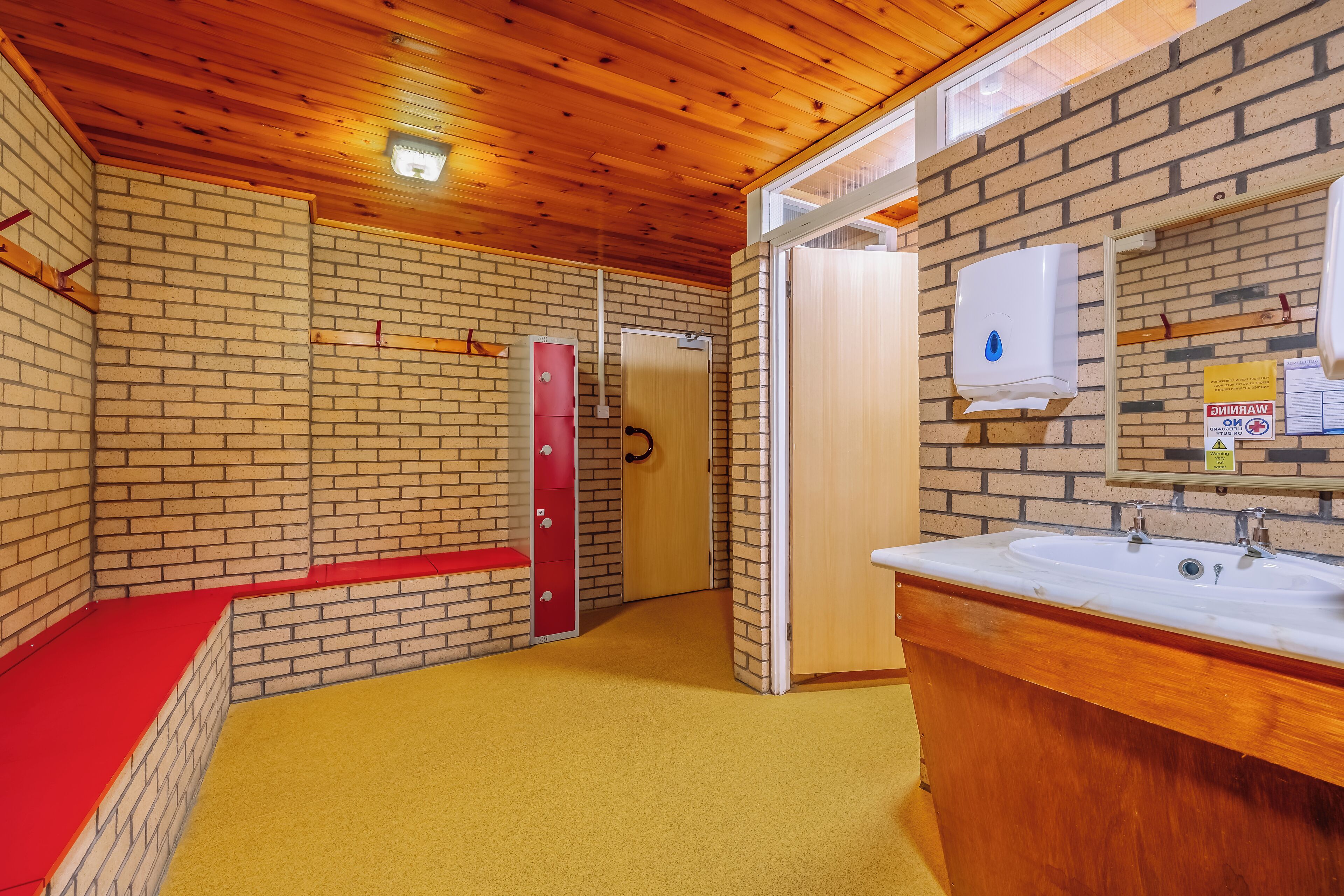 Un baño con techo de madera, un banco rojo, un lavabo y un secador de manos.