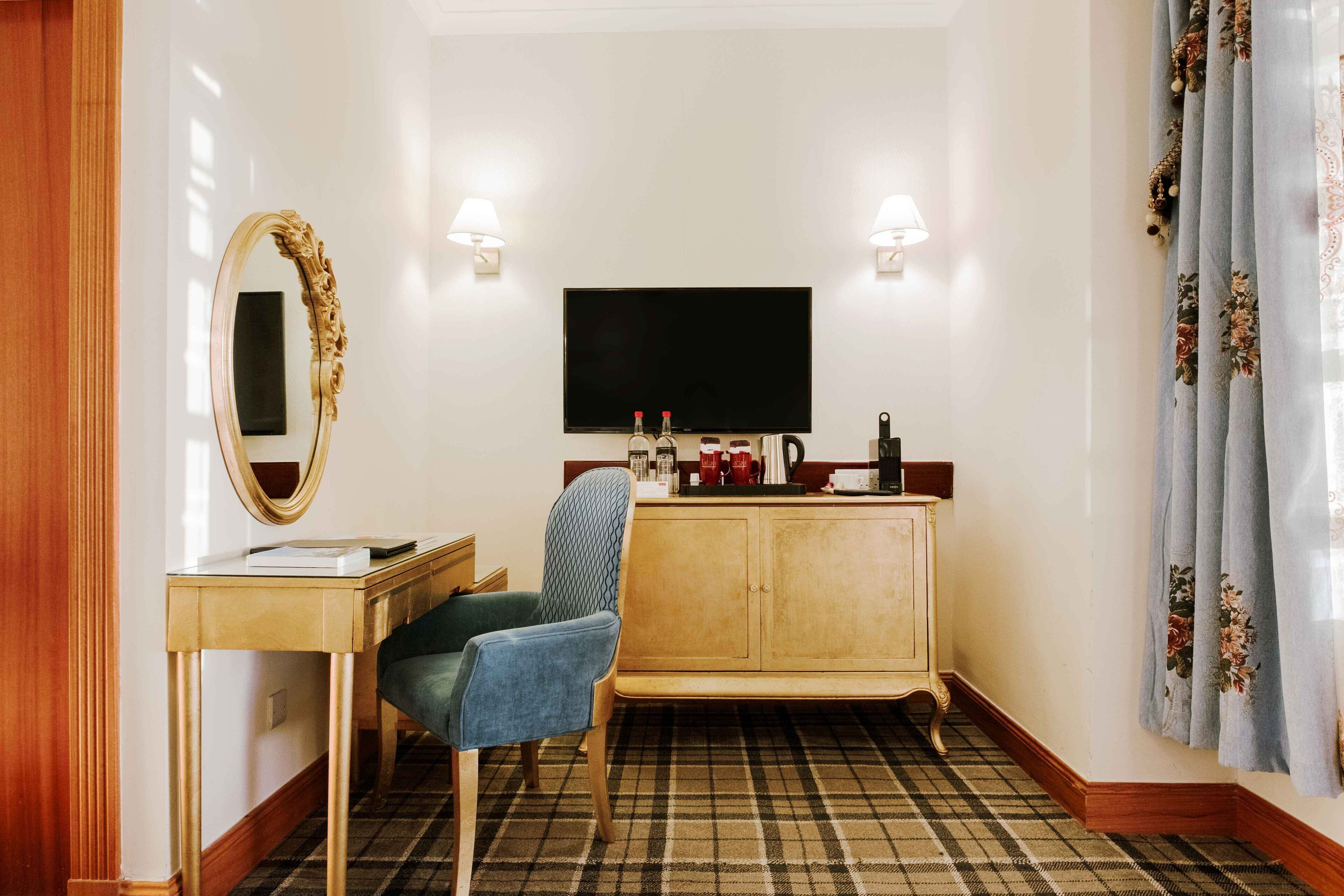 Habitación de hotel con televisión, escritorio con espejo, una silla, un armario y alfombra a cuadros.