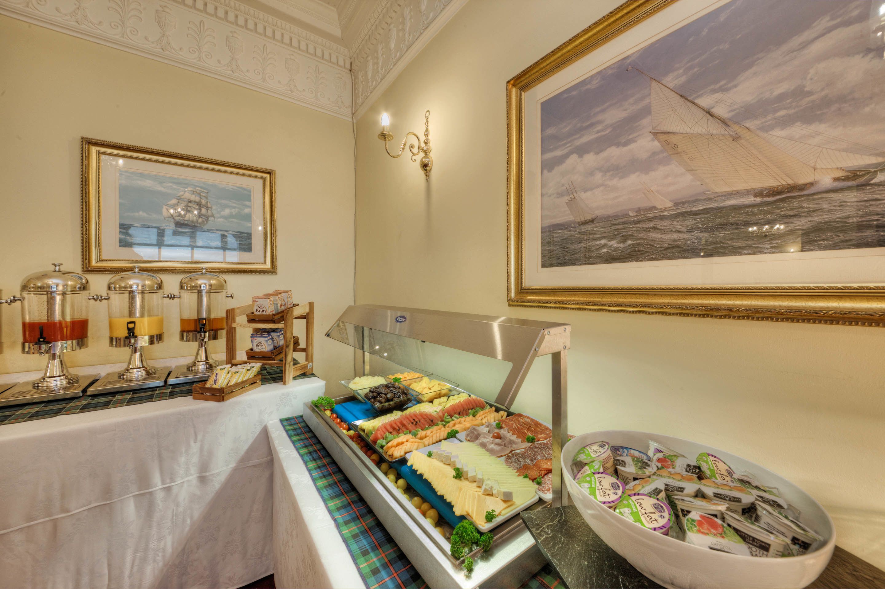 A buffet with various food items, a painting of a sailboat, and a decorative wall sconce.