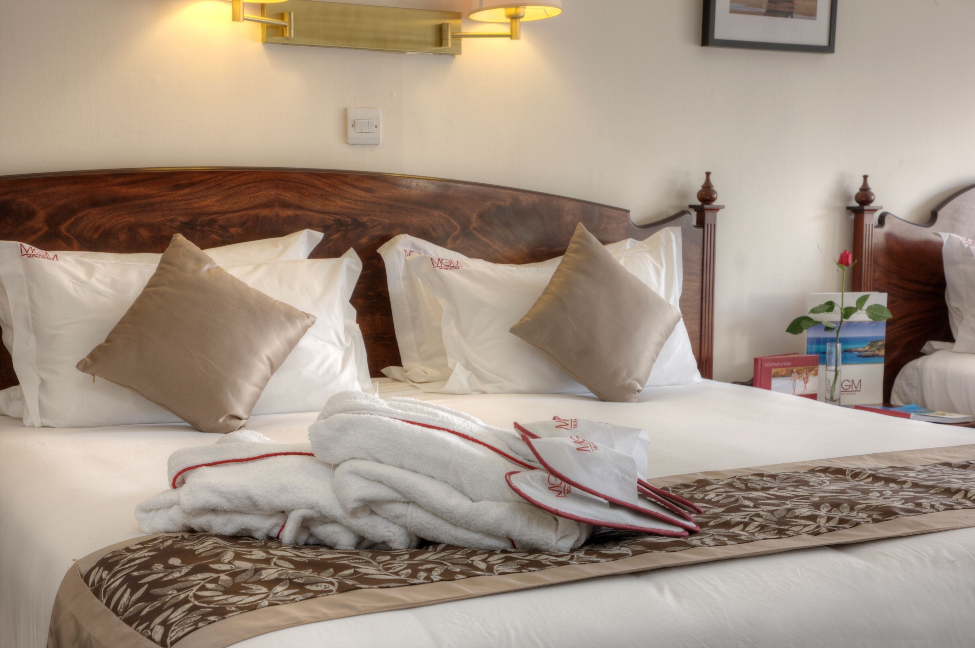 A neatly made bed with a wooden headboard, white and beige pillows, and a floral-patterned throw.