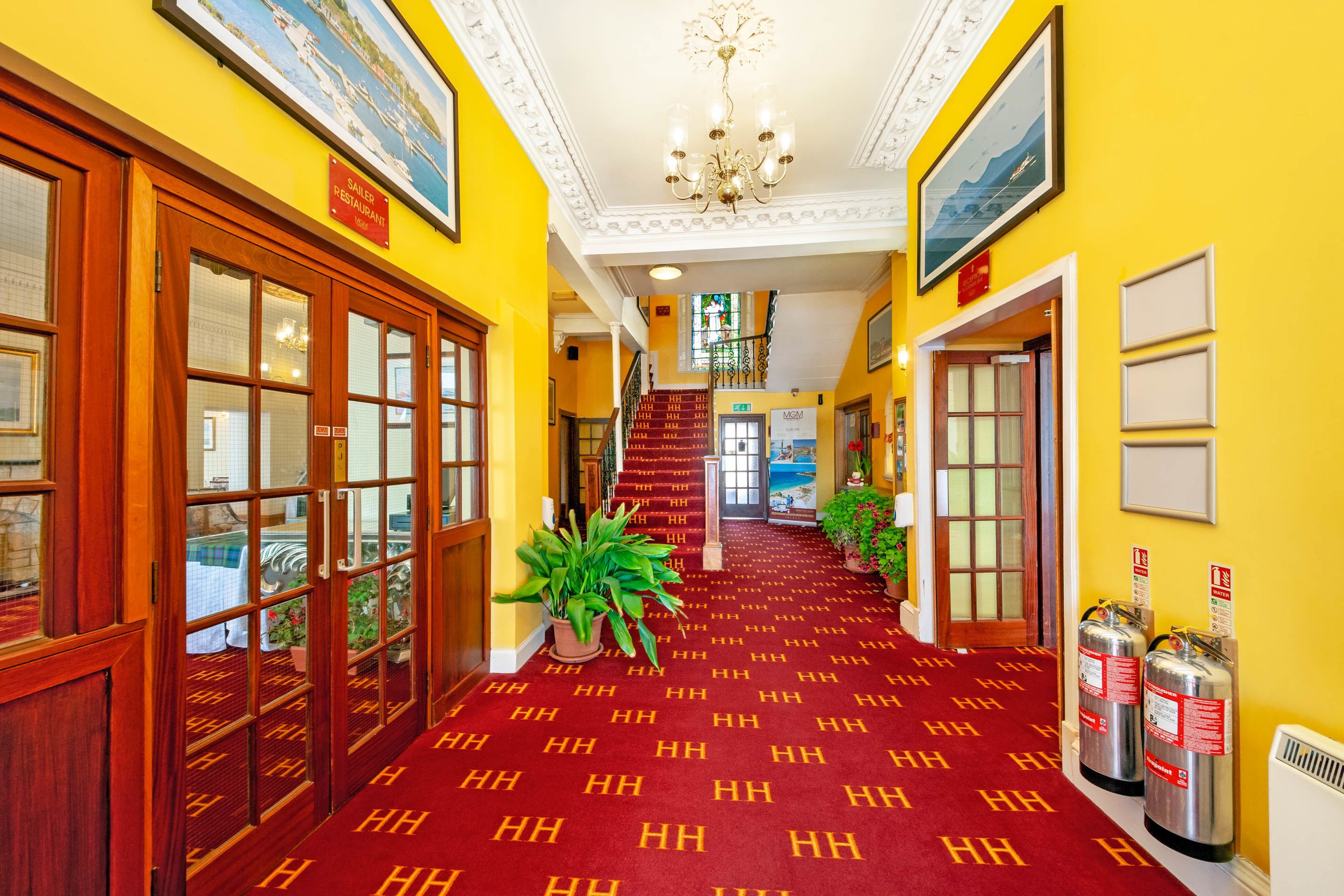 Recepció d'hotel amb una catifa vermella, portes de fusta i una escala que mena a la planta superior.