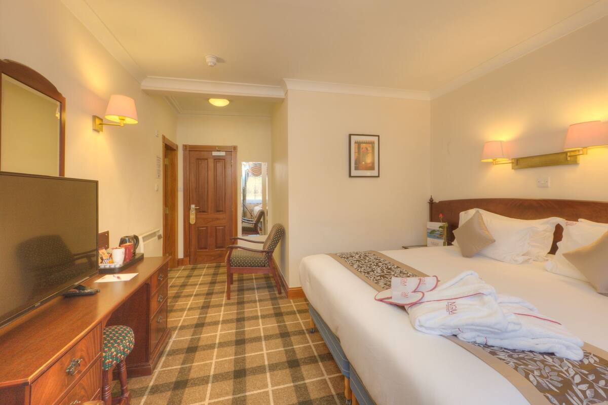 A hotel room with a bed, a desk with a television, a chair, and a check-in counter.
