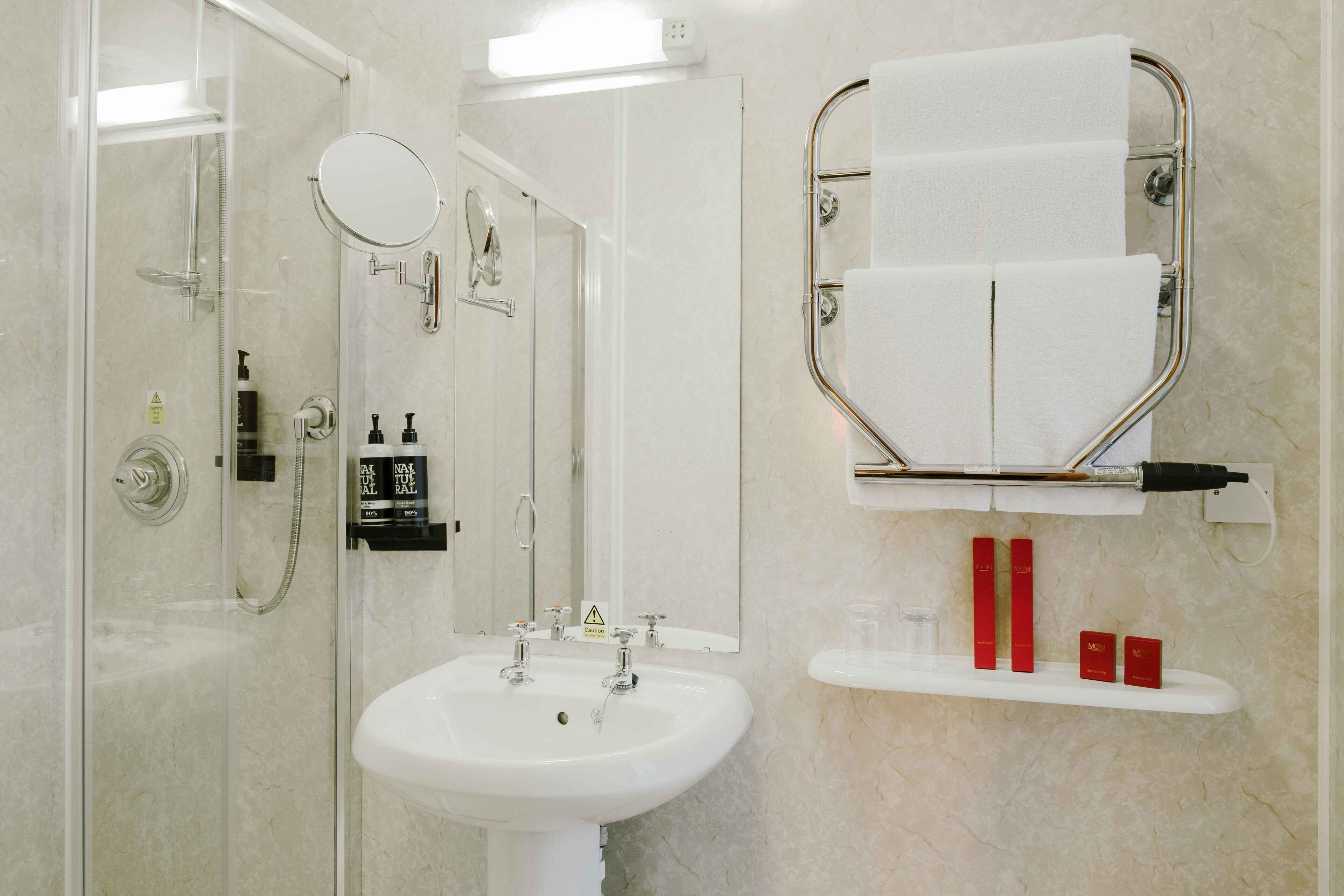 A bathroom with a glass-enclosed shower, a sink, a mirror, and a towel rack.