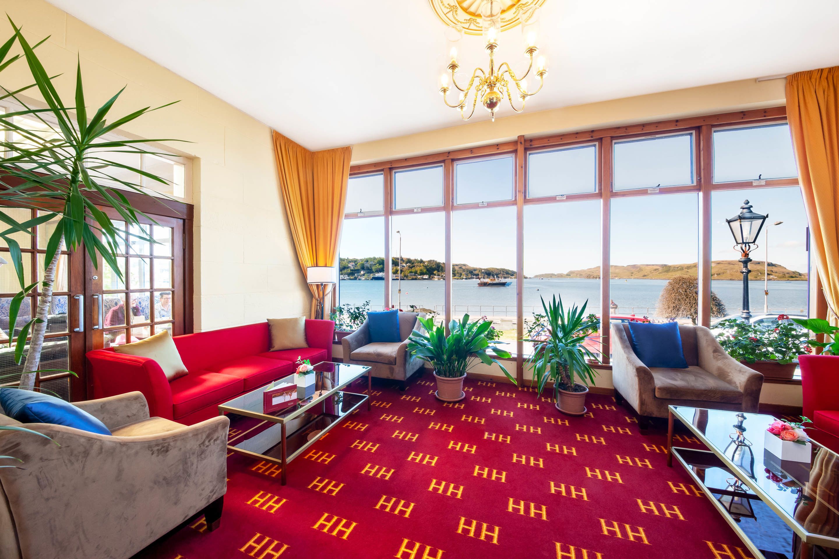 A spacious room with a large window offering a view of the sea, a red carpet, and a chandelier.