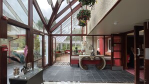 Un amplio espacio interior con techo de cristal, una recepción y una zona de estar con sillas y mesas.